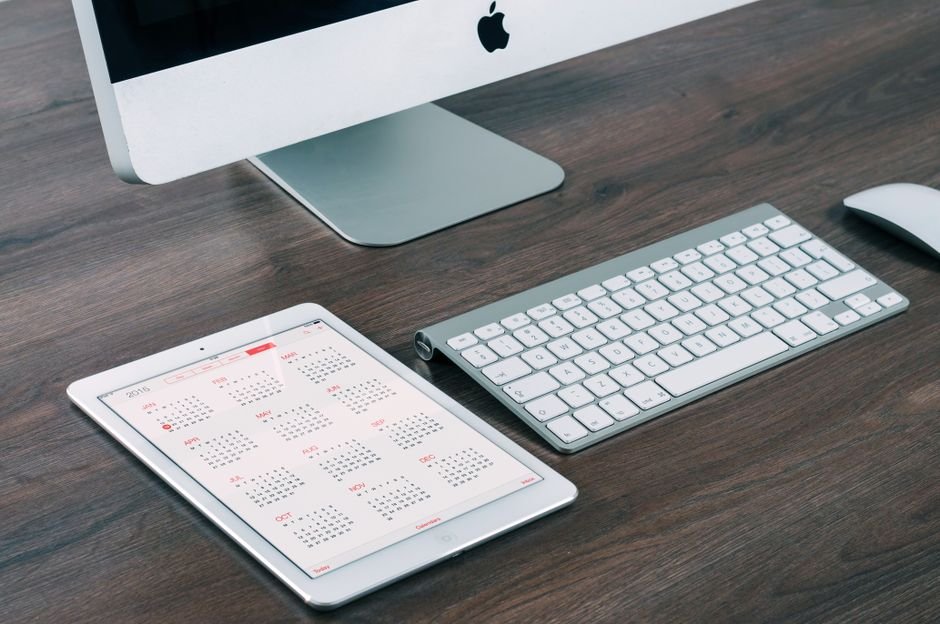 A digital wall calendar displayed on a tablet next to a computer setup, illustrating effective organization tools.