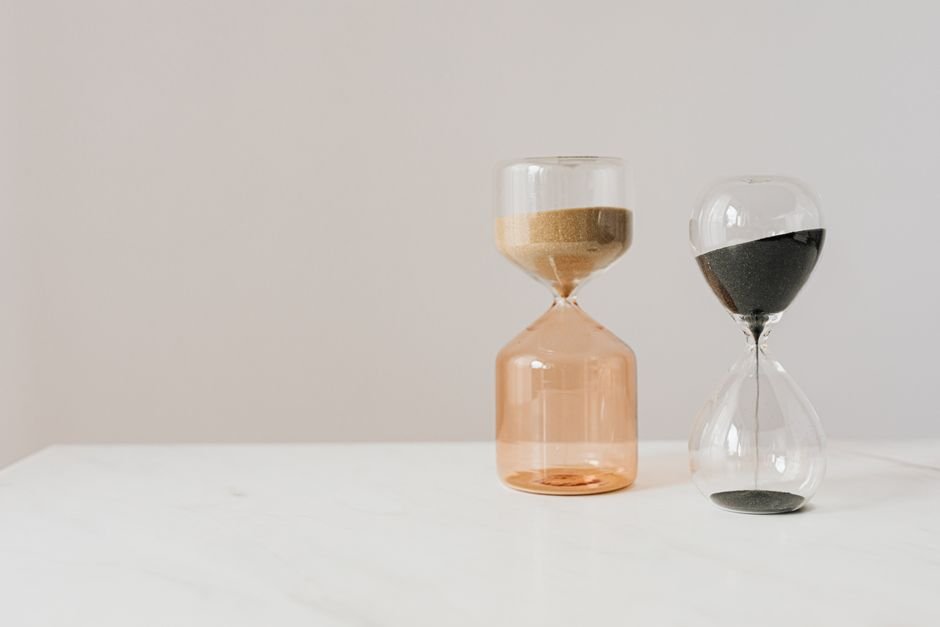 Two hourglass sand timers, one with gold sand and one with black sand, illustrating effective time management tools.
