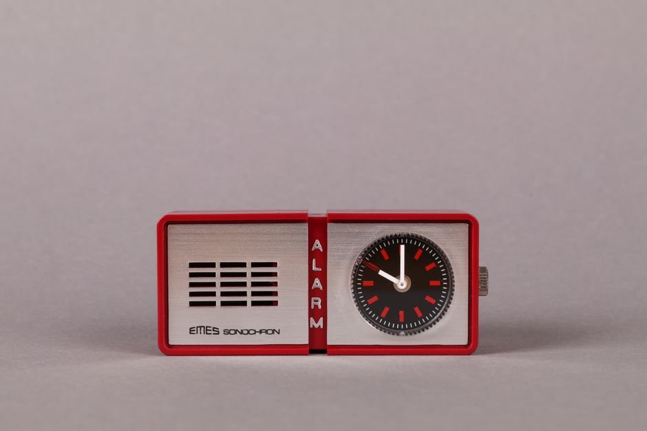 A small red travel alarm clock with a classic design, featured in an article about travel alarm clocks.