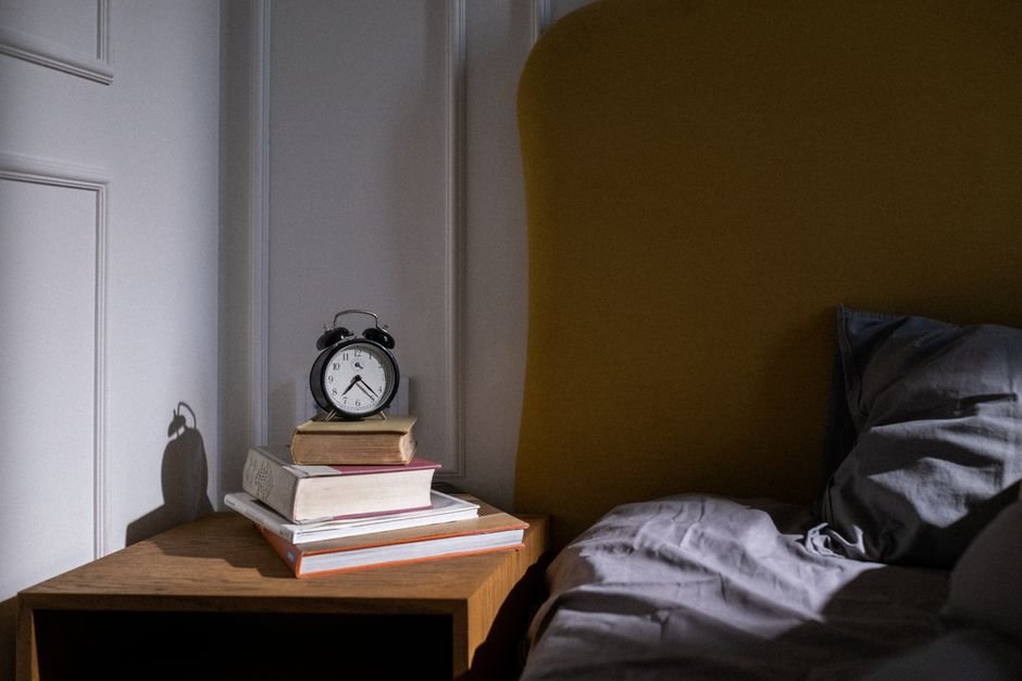 A classic alarm clock on a nightstand with books, illustrating sunrise alarm clocks.