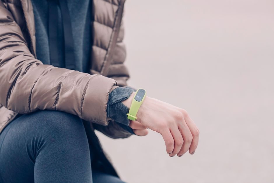 A person wearing a green fitness band on their wrist, illustrating the difference between smartwatches and fitness bands.
