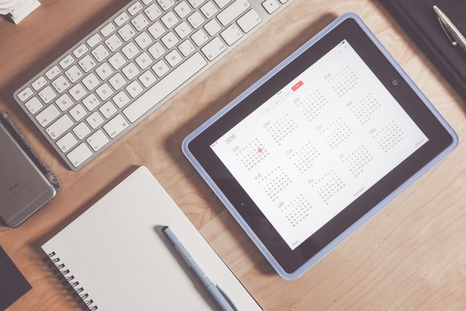 A tablet displaying a digital calendar alongside a keyboard and notebook, relevant to digital wall calendars reviews.