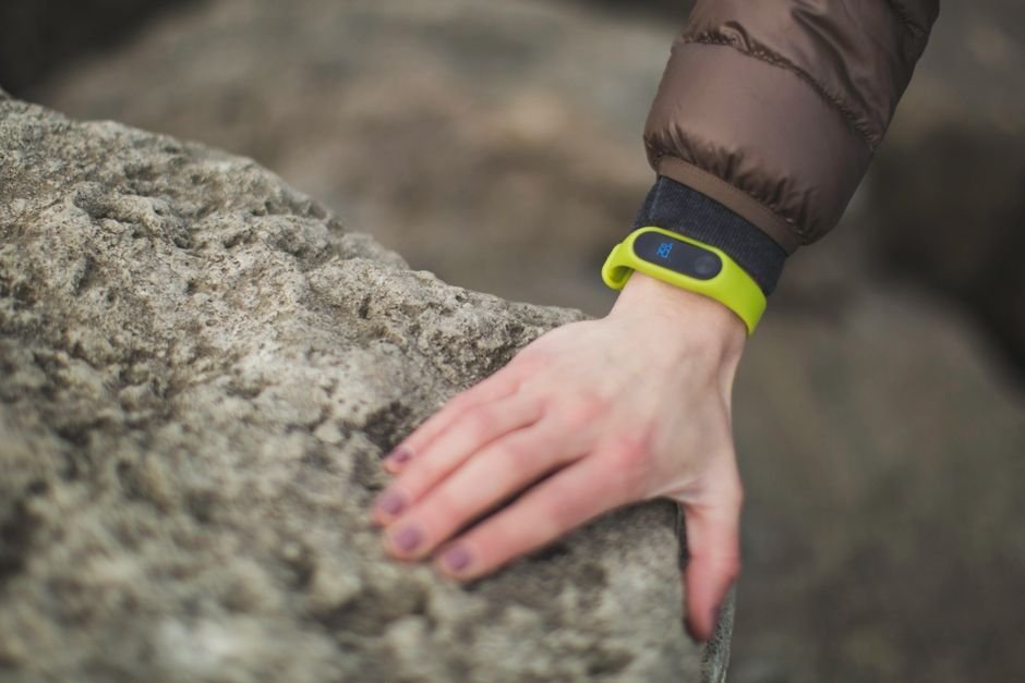 A hand wearing a bright green fitness tracker rests on a rock, illustrating wearable tech for fitness.