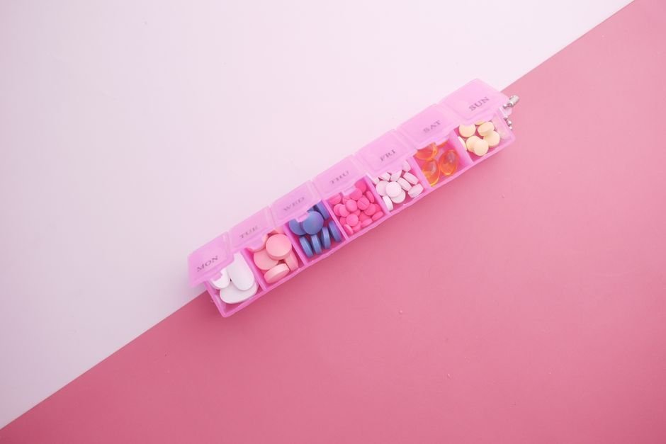 A pink compact pill organizer filled with various colored pills, illustrating the article on pill organizers.