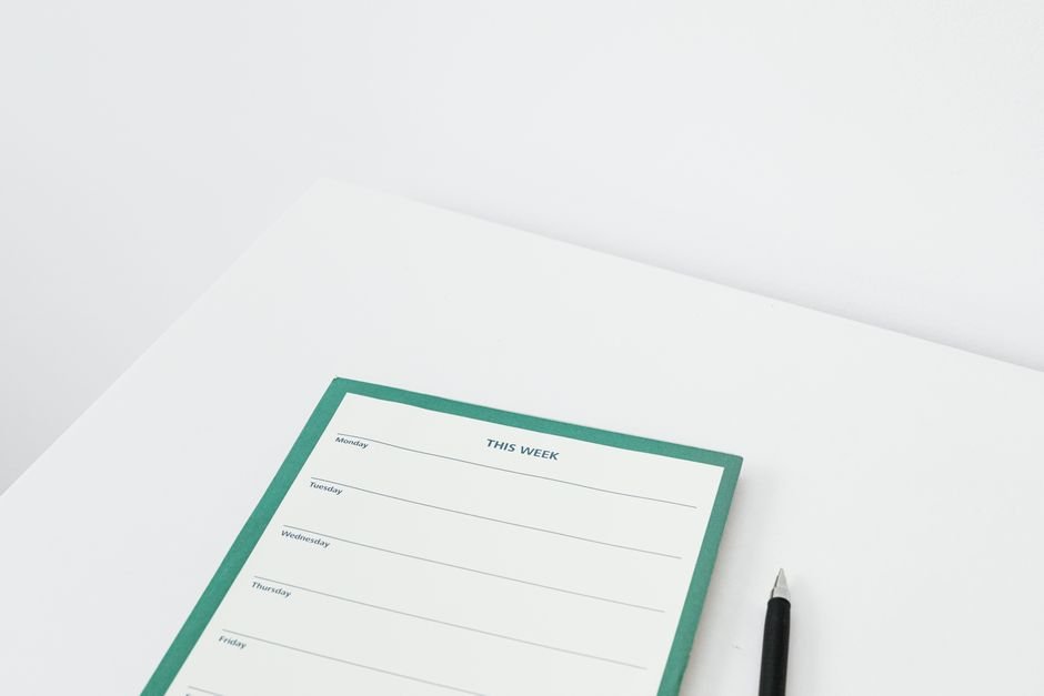 A weekly desk planner with sections for each day, shown on a white table.